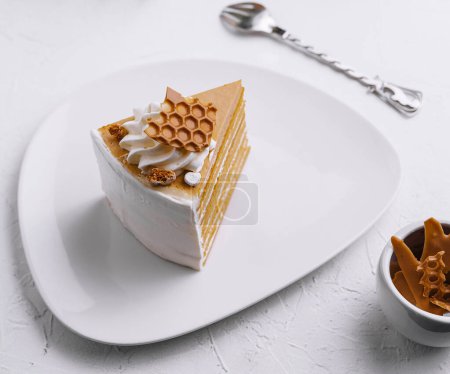 Slice of honey layer cake on a plate beside a full cake with elegant presentation