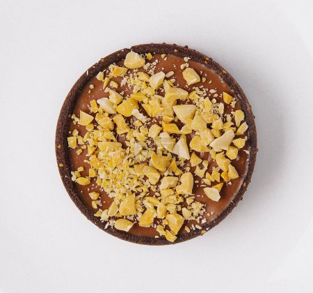 Top view of a single chocolate tart topped with crushed nuts on a clean white plate