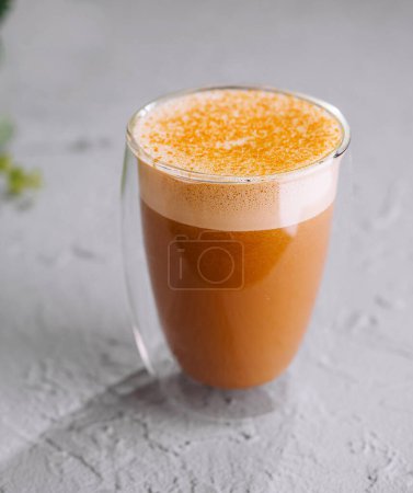 Glass cup of frothy spiced tea latte on a gray textured surface with soft greenery in the background