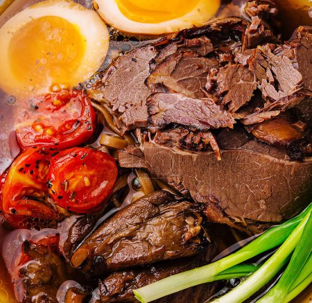 Traditional beef ramen with soft-boiled egg, tomatoes, and green onions in a rich broth