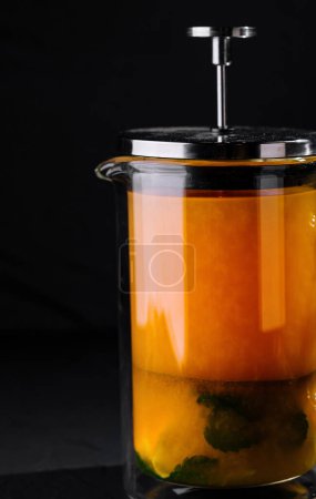 Elegant french press containing vibrant herbal tea, showcased on a dark background