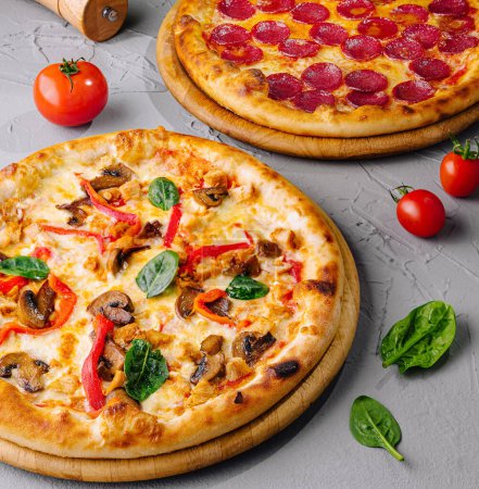 Zwei leckere Pizzen mit Paprika und Gemüse, frische Zutaten auf grauer Oberfläche