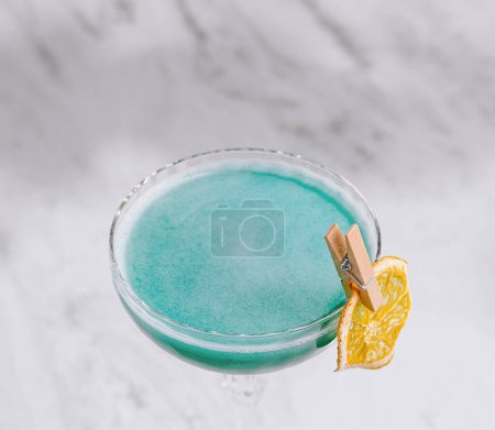 Refrescante cóctel azul en una copa de martini, acentuado con un toque naranja, presentado en una encimera de mármol elegante