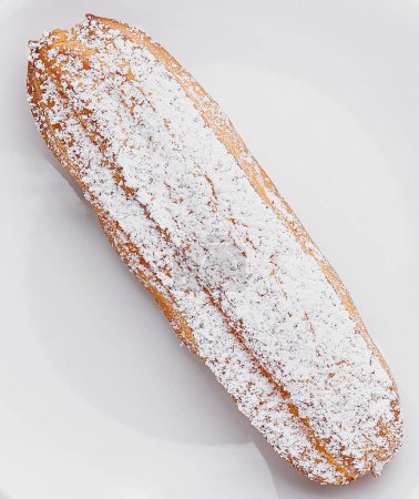 Photo for Appetizing eclair dusted with powdered sugar served on a pristine white plate - Royalty Free Image