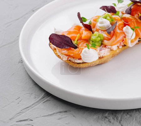 Elegant smoked salmon bruschetta garnished with herbs and cream cheese, presented on a clean white dish