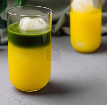 Foto de Vibrante matcha verde flotan junto a un vaso de jugo de mango fresco sobre un fondo gris chic - Imagen libre de derechos