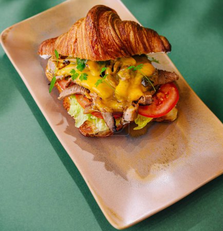 Delicioso sándwich de croissant con rellenos suculentos presentado en un plato elegante