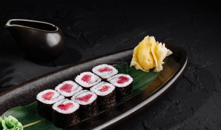 Schön arrangierte Thunfisch-Sushi-Rolle auf Blatt, mit Ingwer und Wasabi, auf glatter schwarzer Oberfläche
