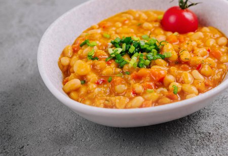 Bowl of hearty chickpea stew garnished with fresh herbs and a cherry tomato on a textured background
