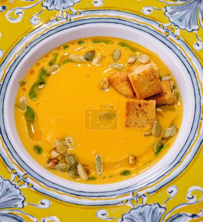 Top-down view of a colorful bowl with creamy pumpkin soup, garnished with seeds and croutons