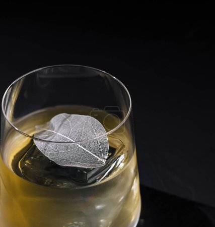 Artistic image of a whiskey glass with ice and decorative silver leaf on a dark background