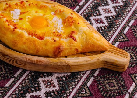 Adjarian khachapuri, a georgian cheese bread, with egg yolk on a rustic patterned tablecloth