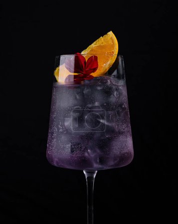 A stylish purple cocktail adorned with citrus and flower on a dark background