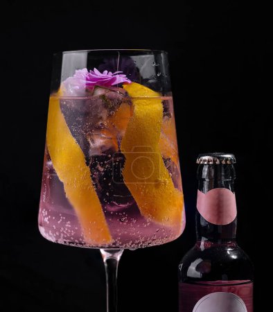 Stylish gin tonic cocktail adorned with a flower and citrus peel on a dark backdrop