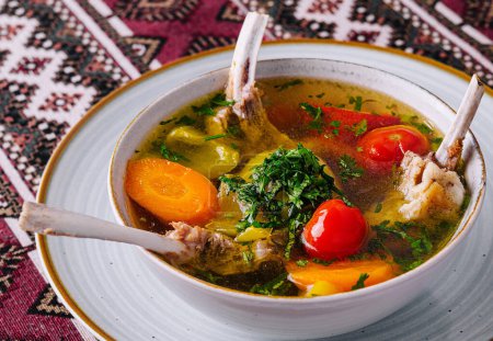 Hearty lamb soup with fresh vegetables, served in a bowl on a vibrant ethnic tablecloth