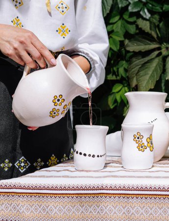 Personne sert une boisson d'un pichet en céramique dans une tasse sur une table avec un décor ethnique