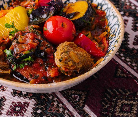 Guiso de uzbek salado con verduras y hierbas mixtas, servido en un tazón decorativo sobre un mantel estampado