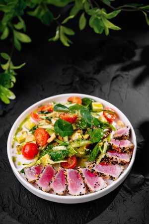 Vibrant bowl of seared tuna salad, garnished with fresh herbs, on a black background