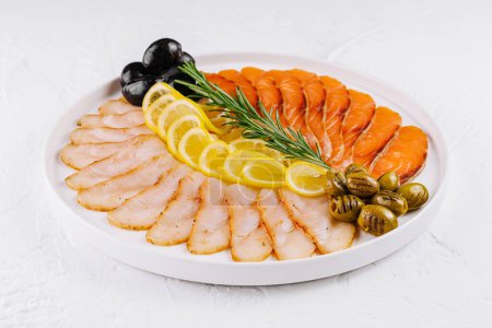Elegant arrangement of smoked fish, including salmon, on a white plate garnished with lemon and capers
