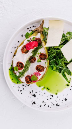 Elegant presentation of a stuffed eggplant dish with arugula, cheese, and sun-dried tomatoes on a white plate
