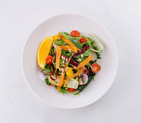 Vibrant bowl of mixed greens with tomato, cucumber, and orange slices on a clean white surface