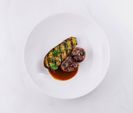 Top view of a succulent steak with grilled zucchini and sauce on a sleek white background