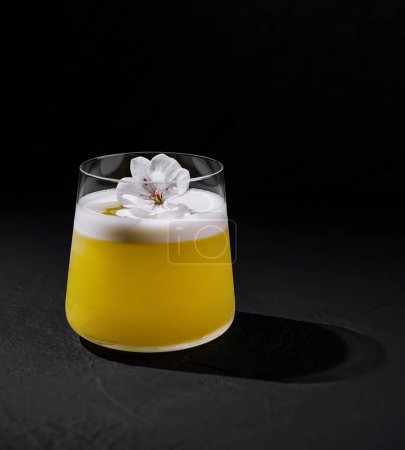 Anspruchsvoller Cocktail mit weißem Blumenschmuck vor dunklem Hintergrund