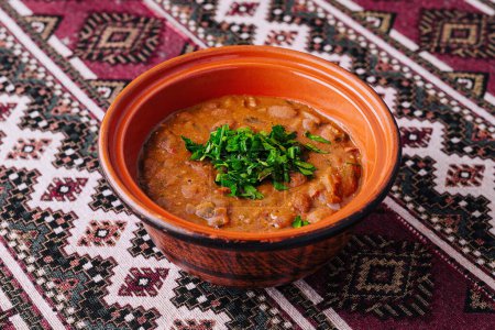 Hearty lentil soup in a rustic clay bowl, garnished with fresh parsley, on an ethnic-patterned tablecloth
