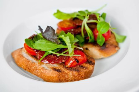 Appetizing bruschetta topped with cherry tomatoes, salad leaves, and a tangy dressing on a white plate