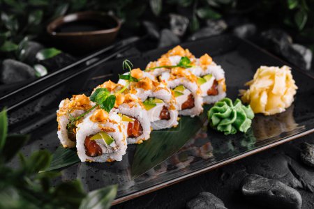 Artystyczna prezentacja sushi z żywymi dodatkami i zdobią elegancką, ciemną płytę pośród kamieni i liści