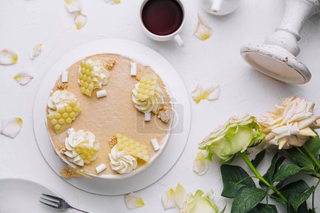 Vista de arriba hacia abajo de un pastel de vainilla bellamente decorado junto con flores frescas y una taza de té