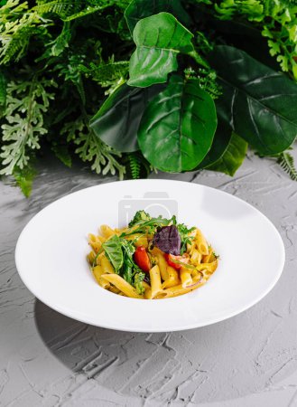 Penne pasta mixed with leafy greens, tomatoes, and herbs, served on a stylish white plate