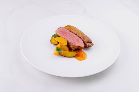 Presentación gastronómica fina de suculenta pechuga de pato emparejada con coloridas verduras sobre un fondo blanco prístino