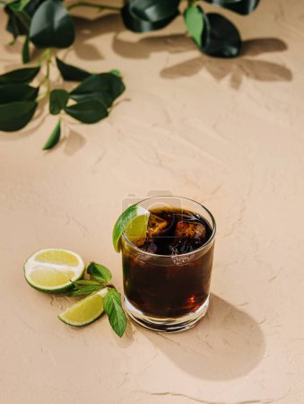 Iced coffee garnished with lime slices and green leaves on a sandy beige surface, evoking a tropical ambiance