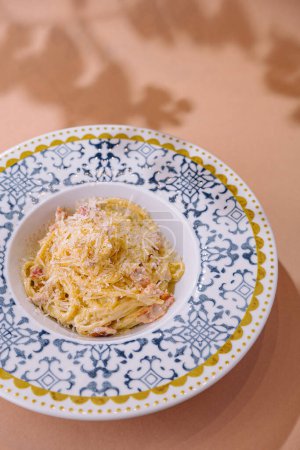 Appetizing plate of spaghetti carbonara garnished with cheese on a patterned plate, with a neutral background