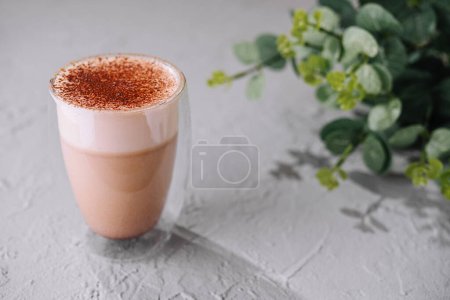 Aromatic milk tea latte topped with spices, served in a clear glass, with a green plant background