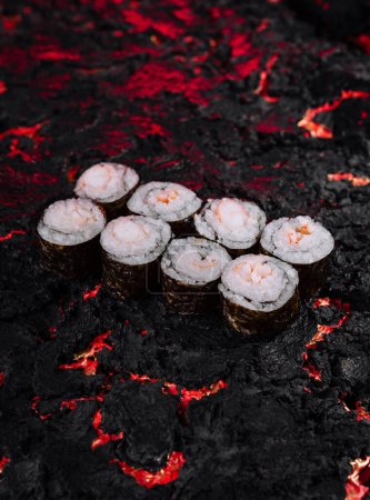 Aesthetic image of sushi rolls arranged on a rugged black lava surface with fiery red highlights