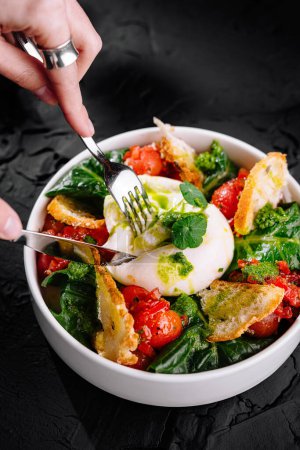 Bowl of burrata cheese salad, with ripe tomatoes, spinach, and crispy bread on black background
