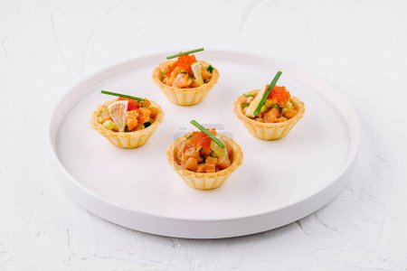 Elegant appetizer tartlets filled with salmon, caviar, and herbs presented on a white plate