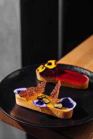 Dessert élégant avec des garnitures vibrantes servies sur une assiette noire élégante, mettant en valeur le style gastronomique