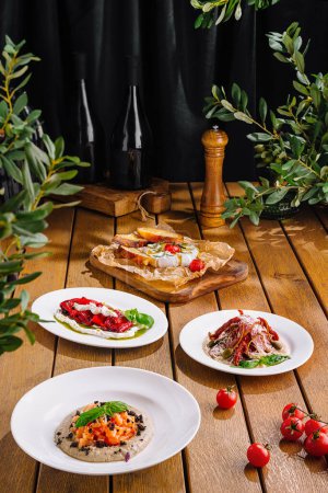 Delicious gourmet italian bruschetta assortment with fresh ingredients on a rustic table with wooden background, wine bottles, and greenery, perfect for casual dining and culinary presentation