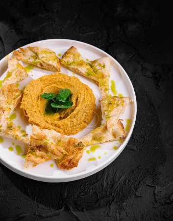 Elegant presentation of smooth hummus with fresh basil, olive oil, and crispy pita on a dark background