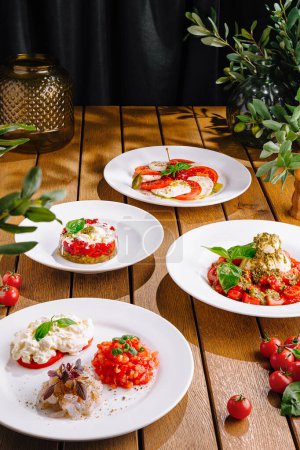 Variety of tomato and cheese dishes artfully presented on white plates, with rustic wood table backdrop