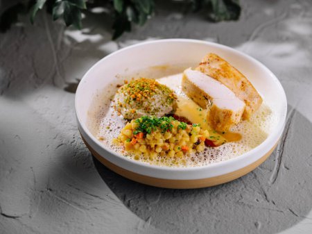 Plate of succulent chicken breast, coupled with spiced couscous and a delicate foam, on a modern table