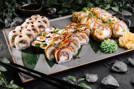 Appetizing array of sushi rolls garnished with sauces, ginger, and wasabi on a slate tray