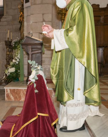 Téléchargez les photos : Prêtre avec une sainte galette à la main, prêt à donner la communion lors d'une messe à l'intérieur d'une église. - en image libre de droit