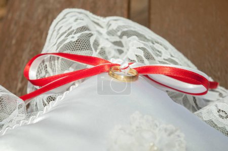 Foto de Anillo de oro anudado con una cinta roja. Un anillo de boda en un pequeño cojín de satén y encaje en el día de la boda. - Imagen libre de derechos