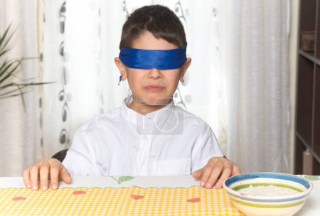 Disgust gesture on the face of an 8-year-old boy after having done a food taste test. Boy sitting with hands on the table blindly tasting food at home.