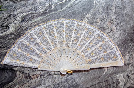 Lace in a white hand fan with gold accents on a gray marble surface.