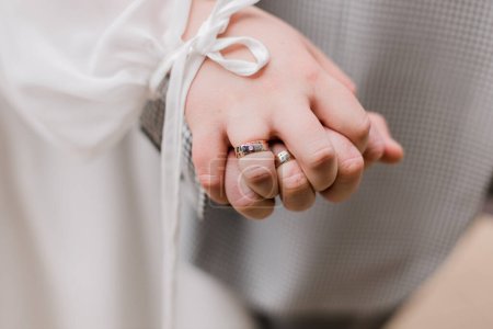 un jeunes mariés se tiennent la main, mettant en valeur leurs élégantes bandes de mariage ensemble